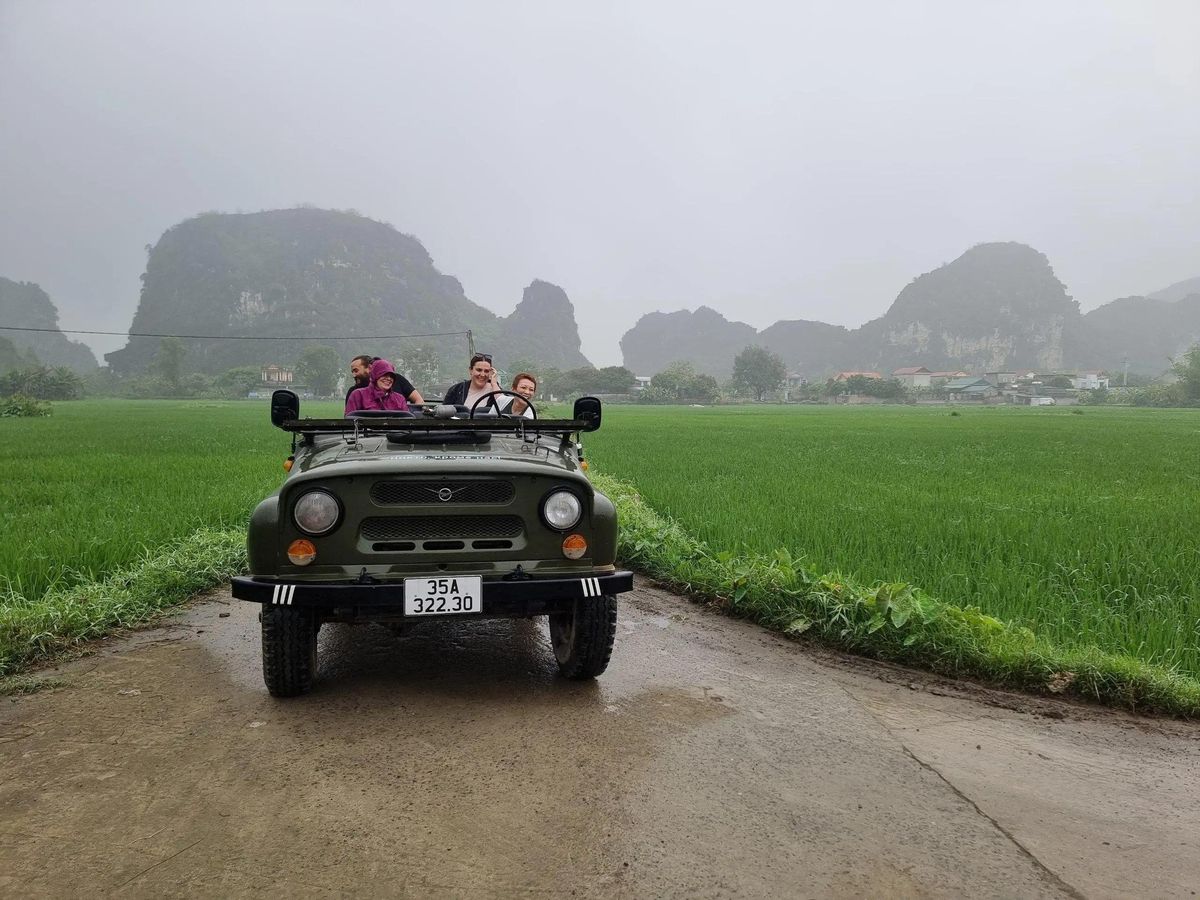 Open-air jeep on a country road through Tam Coc rice fields and limestone mountains — Ninh Binh Jeep Tour